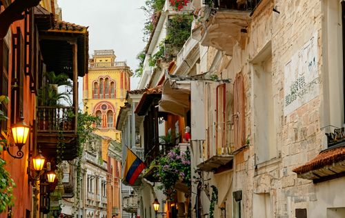 this is the city of cartagena during daylight. This picture was taken in a very colorful street. Featuring vibrant colors such as yellow, green, and orange. This image really sets the vibe and lets the audience kno how vivid and joyful this city is