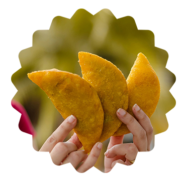 This picture features a beloved street food must called Empanadas. its showing 3 of them being held by a person. the picture was taken outside, this really adds more contrast to the picture and puts the focus on the Empanadas