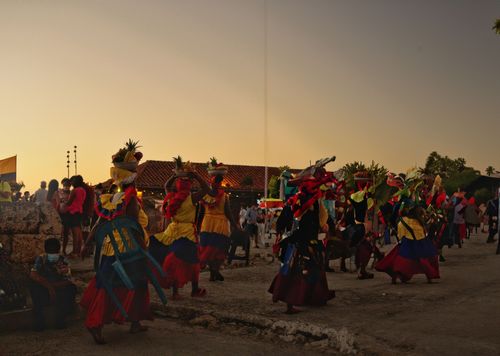 a big gathering during sunsent with 3 women dancing in cultural attire and fruit baskets on their heads